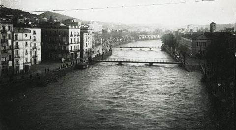 Vista des d'un punt elevat d'una crescuda del riu Onyar. Al centre, el pont del Pes de la Palla i el pont del Carme. A l'esquerra, el carrer del Carme i a la dreta, el convent del M&iacute;nims. 1913-1920
