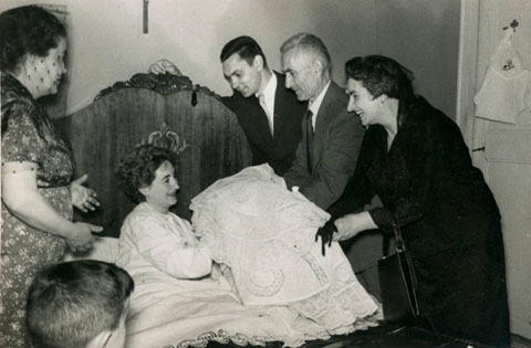 Una mare, al llit, rep el seu fill vestit pel bateig de mans de la llevadora. L'infant &eacute;s Xavier, el fill de Joan Olivas i Roser Recarens, de Banyoles. 1960