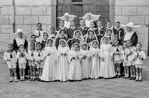 Primera comuni&oacute; dels infants de l'Hospici. Retrat dels infants amb les monges al pati. 1951