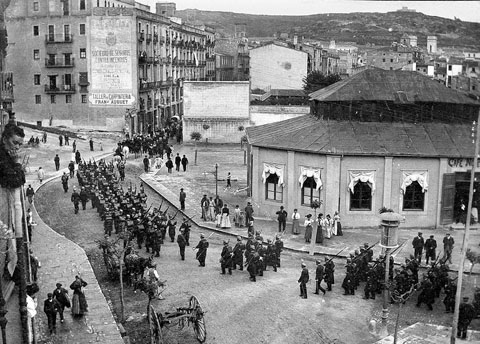 Vista des d'un punt enlairat de la pla&ccedil;a Marqu&egrave;s de Camps i l'encreuament de la Gran Via de Jaume I amb el carrer Nou. Ocupen el carrer un grup de militars que enfilen cap el carrer Nou. A la dreta, el caf&egrave; Novedades. 1900-1910