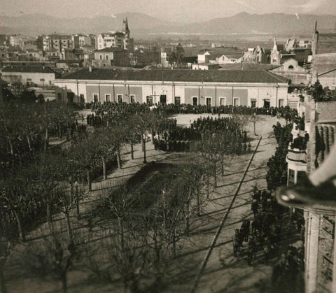Vista des d'un punt elevat de la carretera Barcelona d'una desfilada militar a la pla&ccedil;a del Carril. Davant l'estaci&oacute; de tren, un altar i gent al voltant. Al fons al centre, l'edifici la Punxa i a la dreta, la farinera Teixidor. 1940-1945