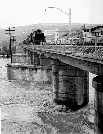 Inundacions a Girona provocades pel desbordament del riu Onyar, Ter i G&uuml;ell. El pont del Ferrocarril amb una locomotora circulant. 13/09/1963