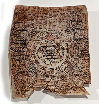 Amulet hebreu. Tinta negra sobre pergam&iacute;. Segle XVIII, Europa de l'Est. A les comunitats jueves medievals era molt com&uacute; l'&uacute;s d'amulets que tenien la funci&oacute; de protegir tant la mare que paria com la criatura que naixia. En aquest s'hi veuen combinacions de lletres de l'alefat que configuren noms divins i d'&agrave;ngels protectors i s'hi llegeix l'expressi&oacute 'ha-eix xaca ha-eix' (el foc s'enfonsa en el foc), un conjur de protecci&oacute; en el moment del part