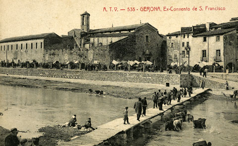 El convent de Sant Francesc de Paula, conegut com els M&iacute;nims, i la palanca de l'Areny vistos de l'altre costat del riu. Paral&middot;lel al riu, el passeig General Mendoza ple de carruatges durant un dia de mercat i a la dreta, la rambla Pi i Margall. S'observen bugaderes rentant roba al riu. 1905
