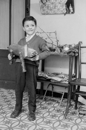 Retrat d'un nen en un interior amb un Ti&oacute; de Nadal a les mans. 1960