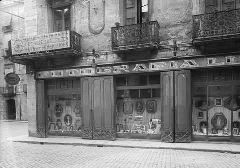 Fa&ccedil;ana i aparador de la galeria Foto Lux en la cantonada amb el carrers Ciutadans. Sobre la galeria hi ha el local de la Secci&oacute; Femenina de la Falange. 1950