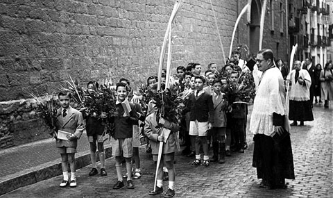 Escolania del Mercadal participant en la process&oacute; de Rams pels carrers de la ciutat. Retrat dels alumnes de l'escolania amb palmons i llorer, acompanyats per moss&egrave;n Ferran Forns, al seu pas pel carrer Obra. 1954