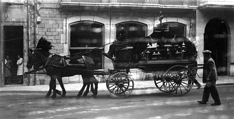 Carruatge f&uacute;nebre tirat per cavalls engalanats circulant per la pla&ccedil;a del Vi a l'altura de l'ajuntament de Girona. 1920