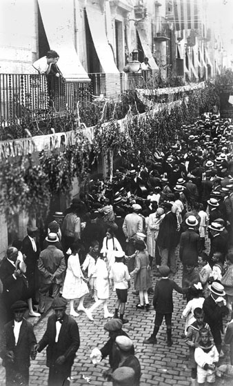 Celebraci&oacute; de la festivitat de Santa Anna al carrer Ballesteries, engalanat amb serrells de paper i branques de boix. Al centre, una cobla tocant sardanes a l'altura de la Casa Mas&oacute;. 1917