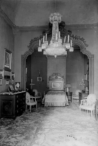 Dormitori senyorial de la casa Carles. Del mobiliari i la decoraci&oacute; en destaquen el llit amb cap&ccedil;alera, la calaixera, les cadires, els quadres i la l&agrave;mpada del sostre. 1911-1915