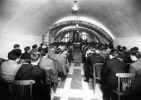 Reuni&oacute; dels membres de la Federaci&oacute; de Joves Cristians de Catalunya (FJCC), coneguts com fejocistes, a la casa Carles, amb l'assist&egrave;ncia del bisbe Josep Carta&ntilde;&agrave;. Presideix la sala una imatge del Sagrat Cor de Jes&uacute;s. 1936
