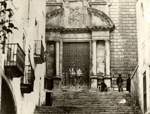 Porta principal de l'esgl&eacute;sia de Sant Mart&iacute; Sacosta. En primer terme, l'escalinata que d&oacute;na acc&eacute;s al temple. S'observen tres persones, una de les quals, la de la dreta, &eacute;s el gu&agrave;rdia de la pres&oacute;. 1870-1880