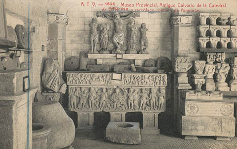 Galeria del claustre del monestir de Sant Pere de Galligants habilitada com a sala del Museu Arqueol&ograve;gic Provincial a Girona. S'observa l'antic calvari de la Catedral de Girona i un sarc&ograve;fag rom&agrave;. 1910-1920
