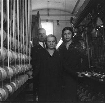Interiors de la f&agrave;brica Grober. Retrat d'un home i dos dones entre les m&agrave;quines.