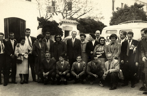 Celebraci&oacute; de la festa de l'Arc&agrave;ngel Gabriel, patr&oacute; dels radiofonistes. Retrat de grup dels treballadors de Radio Gerona EAJ38 i altres assistents davant d'un restaurant d'un lloc no identificat. S'identifiquen, ajupits, el primer a l'esquerra, Emilio Banda. Drets, la setena a la dreta, Francina Boris, el sis&egrave;, Miquel Vidal i el primer a la dreta, Jaume Teixidor. 1955